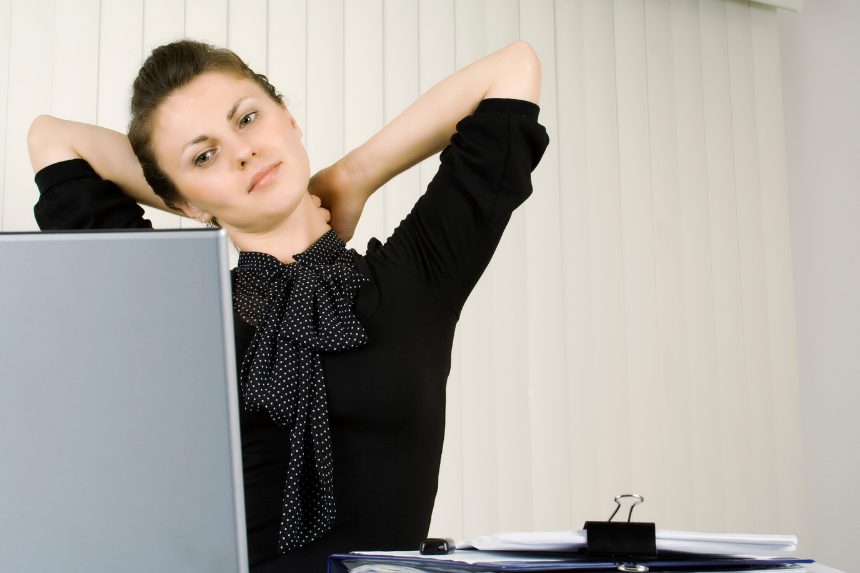 A woman stretches her neck and shoulders while working at a laptop